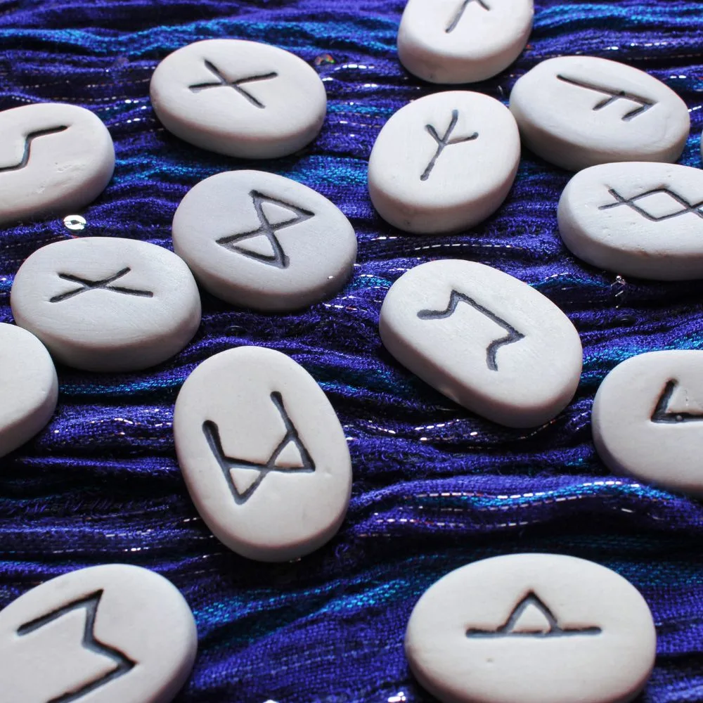 A set of white rune stones with engraved black symbols spread across a textured blue and purple fabric background.
