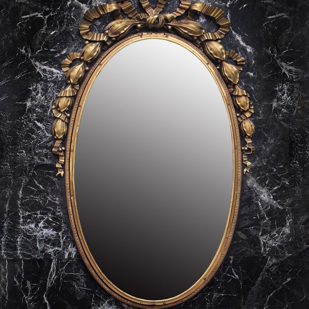 An ornate oval mirror with a gold floral frame mounted on a black marble wall, often used in scrying or mirror gazing practices.