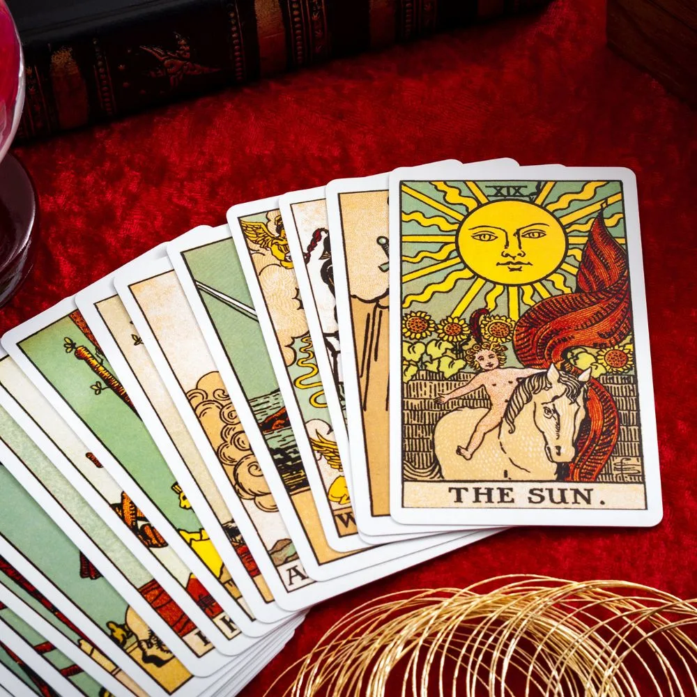 A spread of Rider-Waite tarot cards laid out on a red velvet surface, with "The Sun" card prominently displayed on top. A crystal ball and golden wire decoration are partially visible nearby.