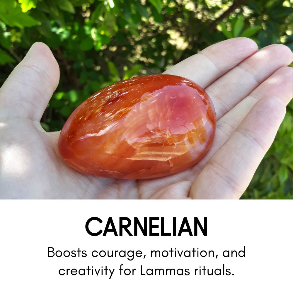 Polished carnelian stone held in an open palm with green leaves in the background. Text below reads: 'Carnelian – Boosts courage, motivation, and creativity for Lammas rituals.'