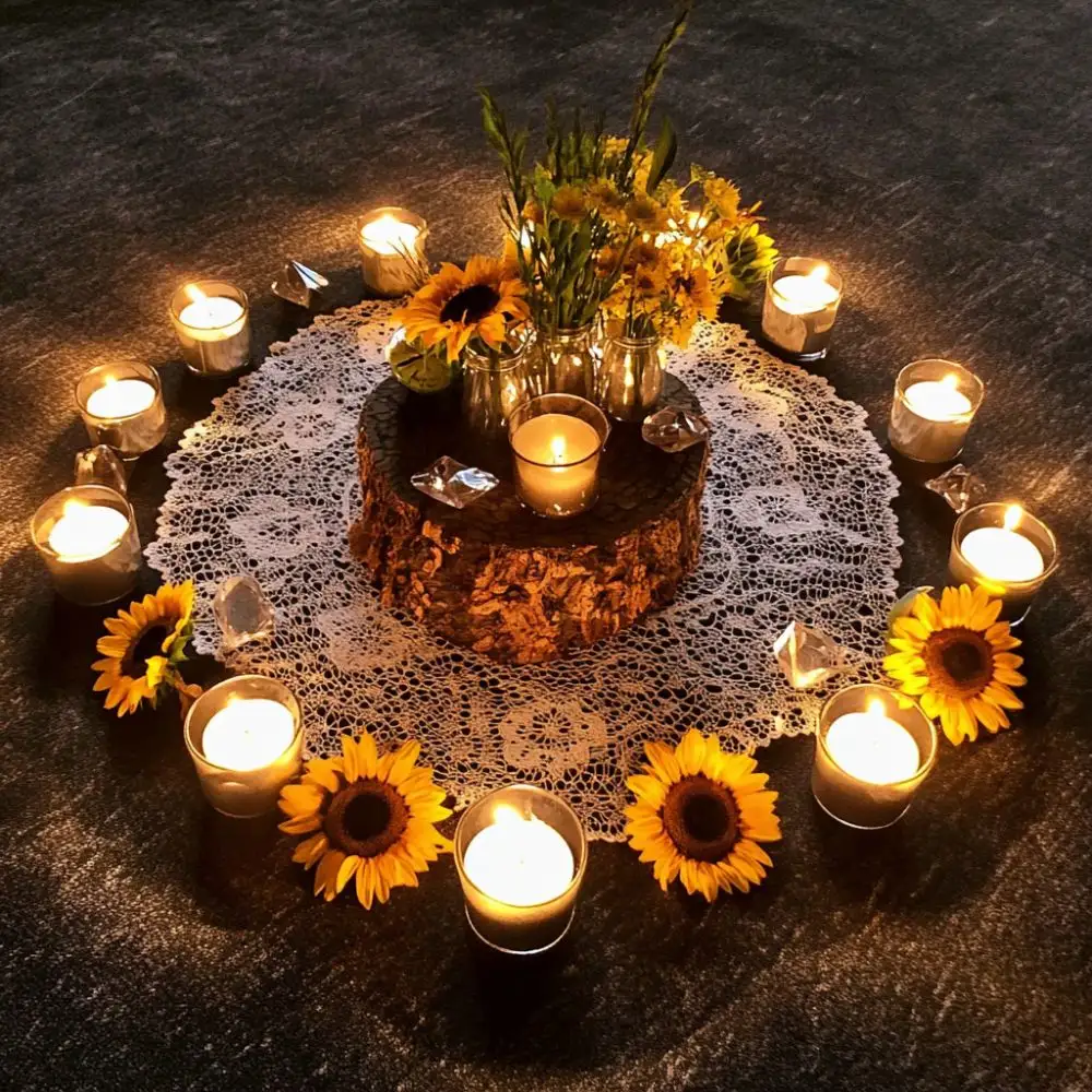 Lammas candle circle with sunflowers, glass jars, and crystals arranged around a tree stump on a lace doily, glowing warmly in low light.